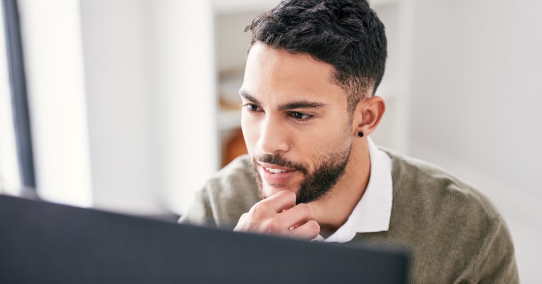 A young man stares thoughtfully at a computer screen.